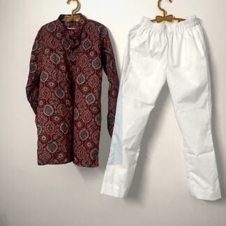 Maroon ajrakh-print cotton kurta and white pyjama hanging on wooden hangers